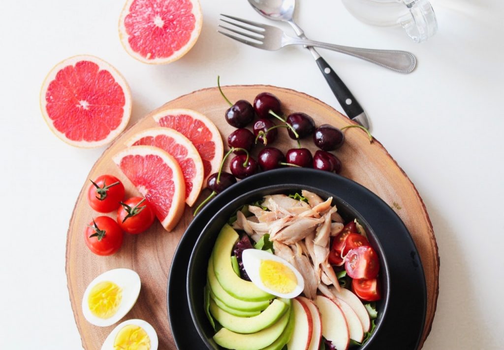 bol sur plateau en bois avec avocat oeuf poulet à côté oeufs pamplemousse et cerises