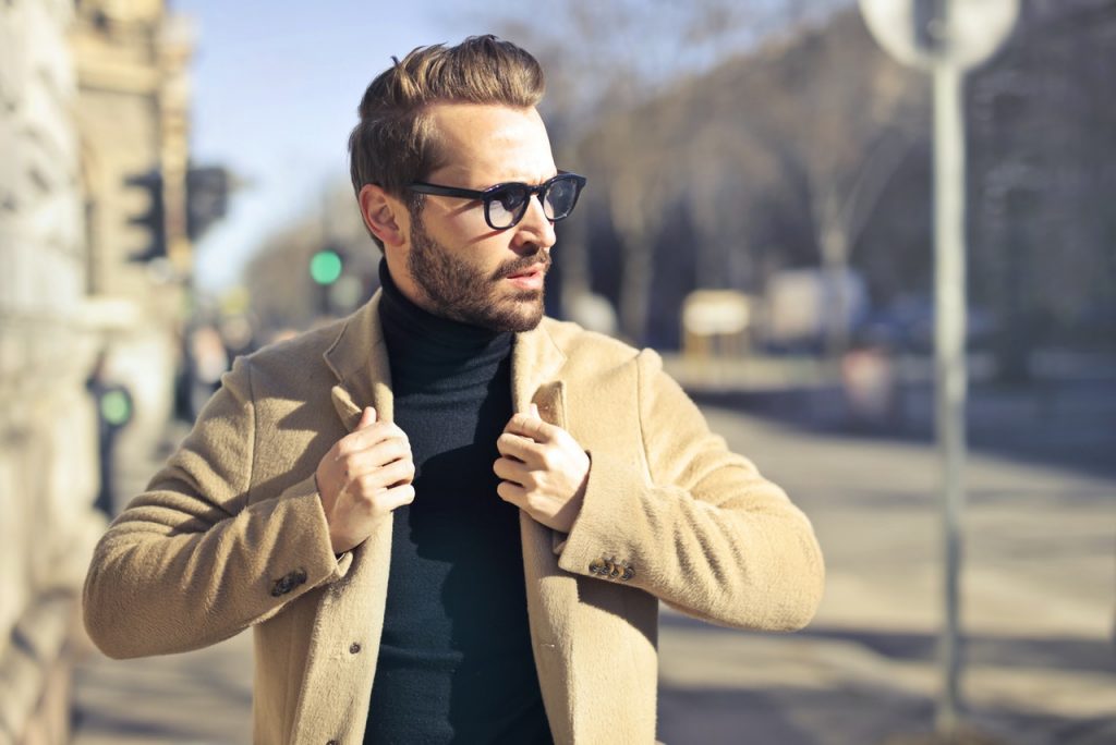 homme avec des lunettes portant un pull à col roulé noir et un manteau beige